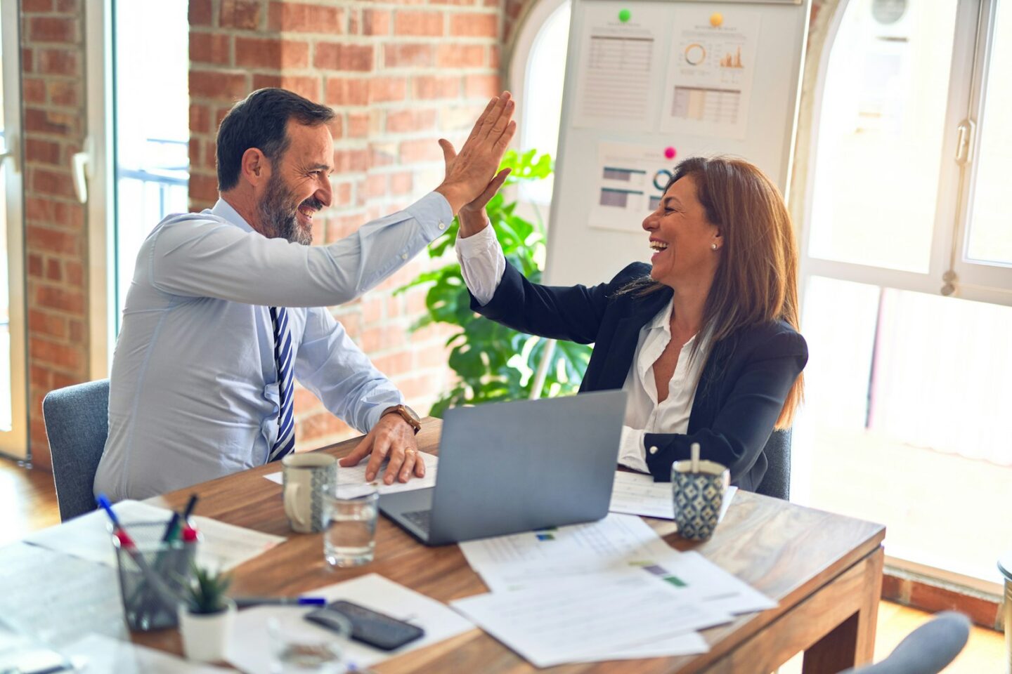 Two colleagues celebrating with a high five at a shared desk (stock photo, not the HelloHRM team)